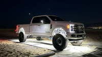 Pure white rock lights glowing under lifted truck on sand at night